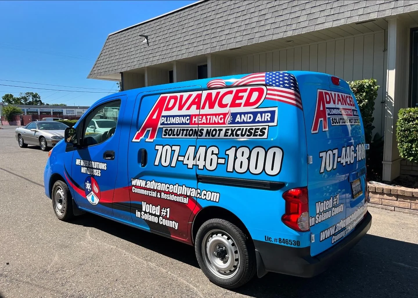 Blue commercial van with advertising for Advanced Plumbing Heating and Air, including phone number and website, parked in a lot with other cars and a building in the background.