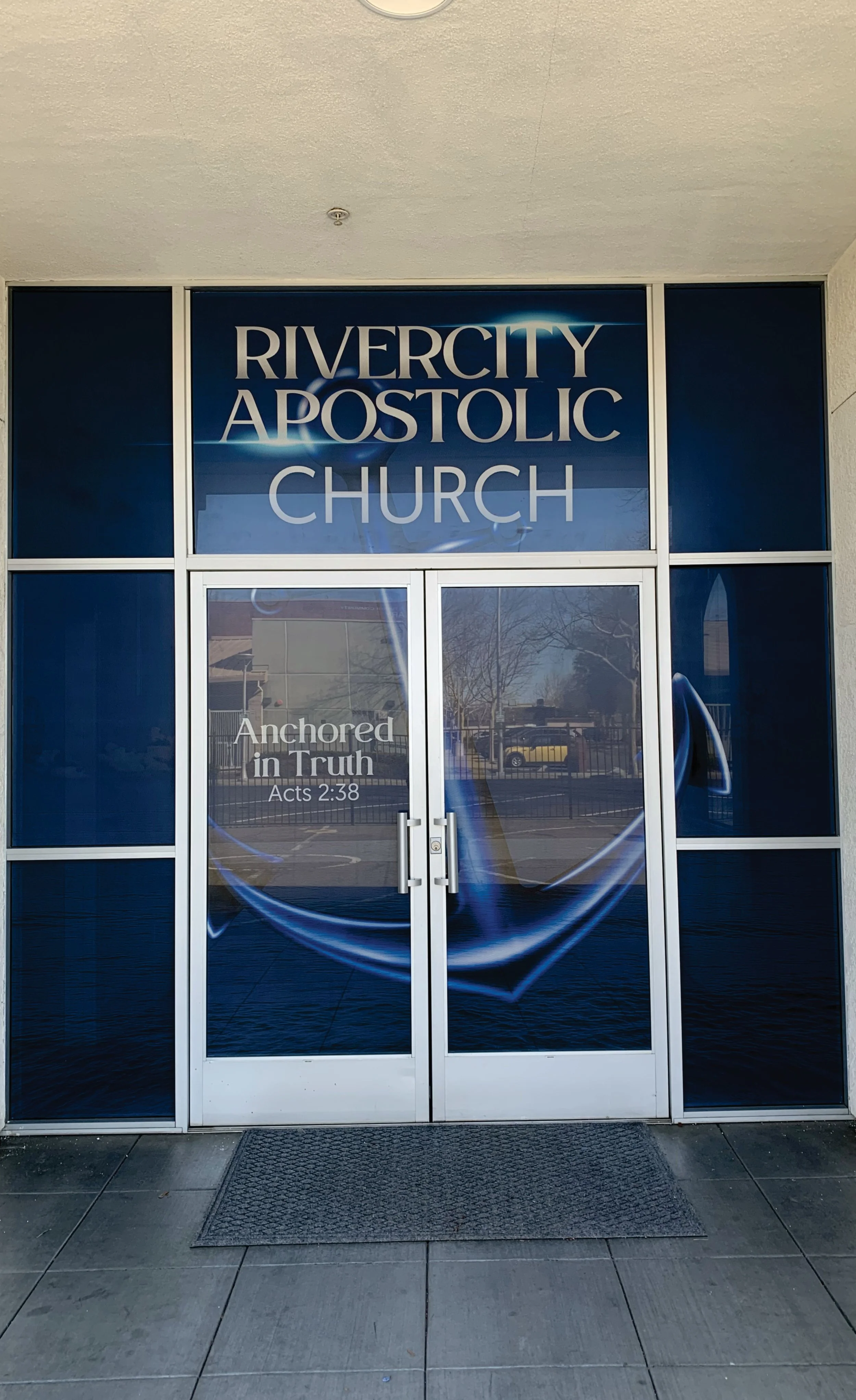 Entrance to Rivercity Apostolic Church with sign stating "Anchored in Truth, Acts 2:38" on glass door.