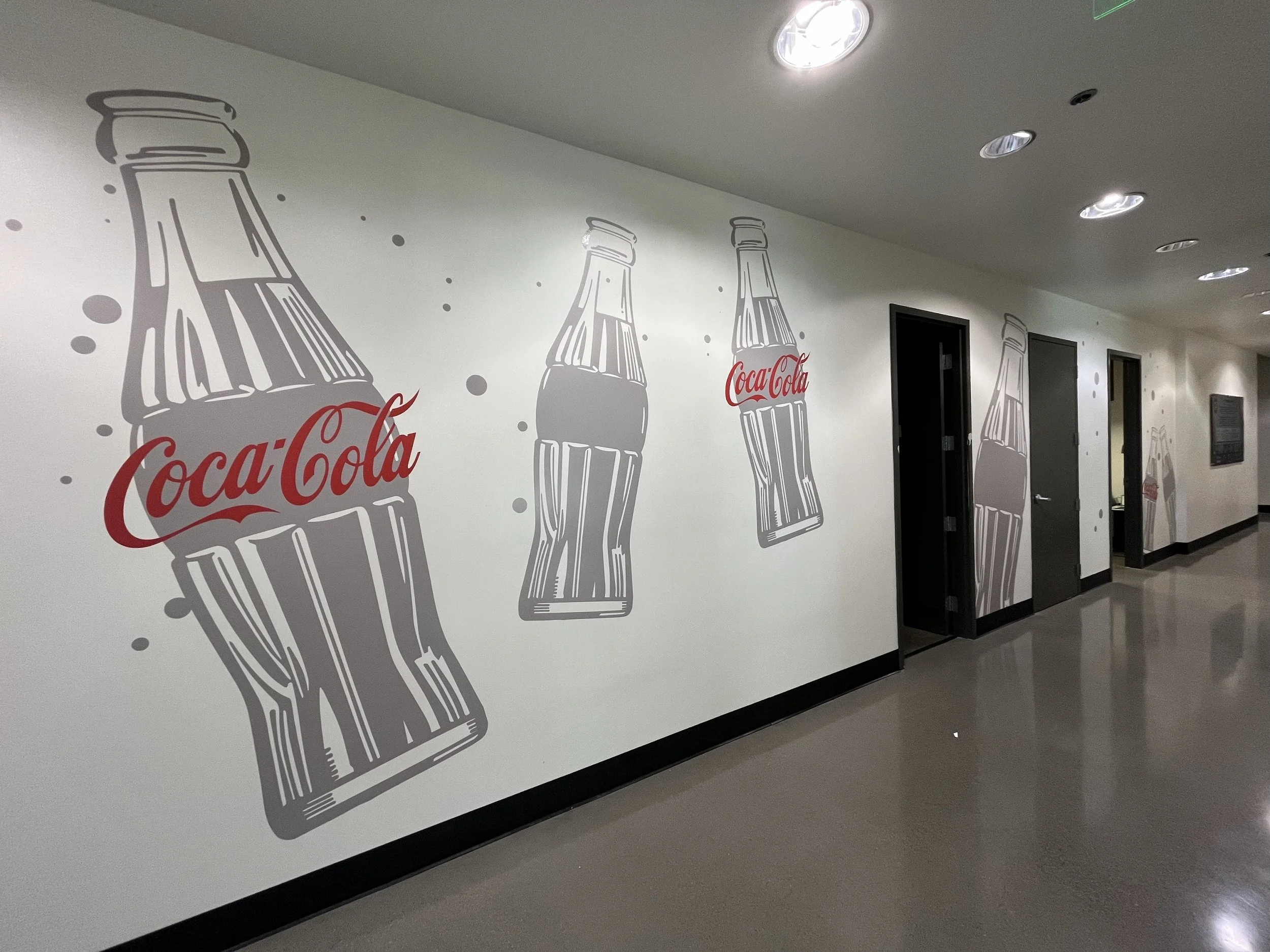 Hallway with white wall decorated with gray and red motivational artwork featuring Coca-Cola bottles with the logo in red.
