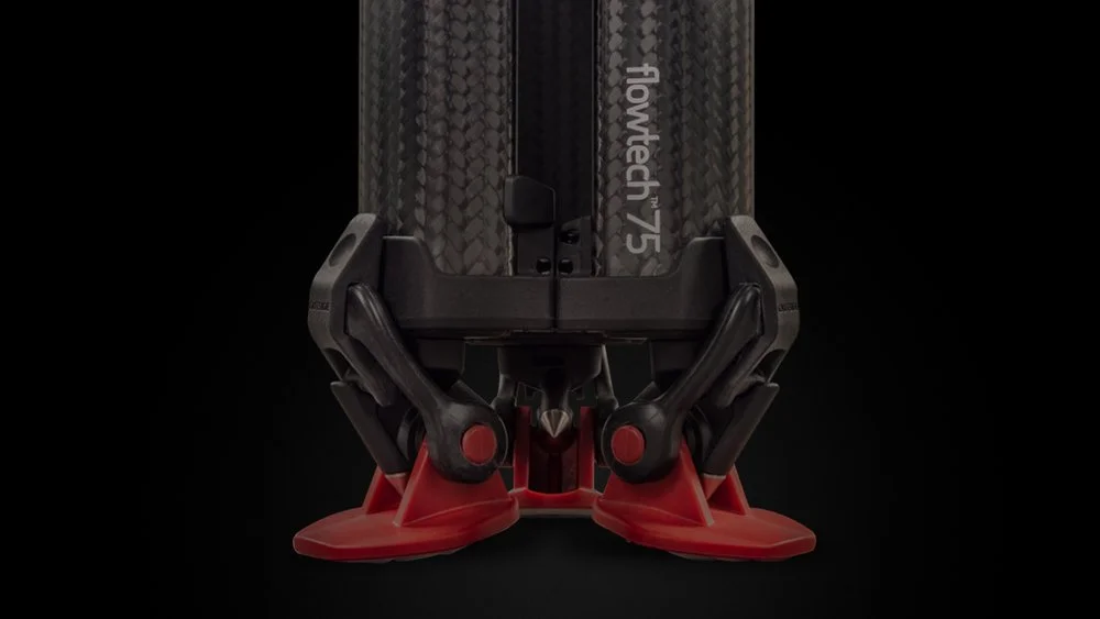 Close-up of a Flowtech 75 turbocharger, showing the black carbon fiber housing, black mounting brackets, and red silicone couplers in a dark background.