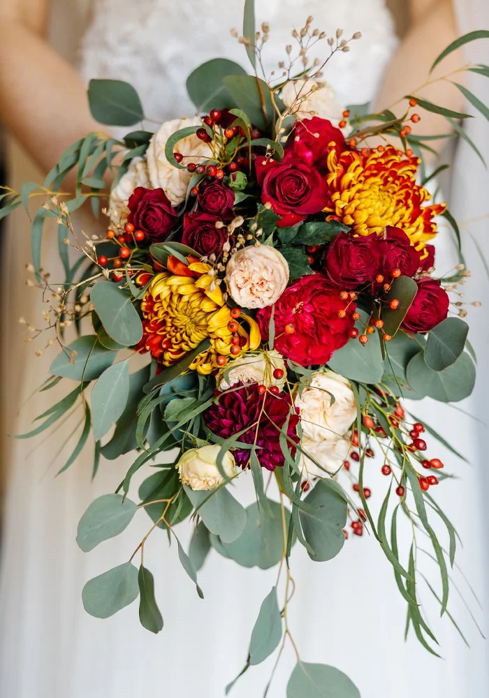 A bouquet of red, yellow, and white flowers with green leaves and small red berries.