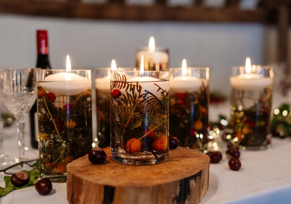 Candlelit glasses with berry and plant decorations on a wooden slice, with a Christmas or holiday theme.