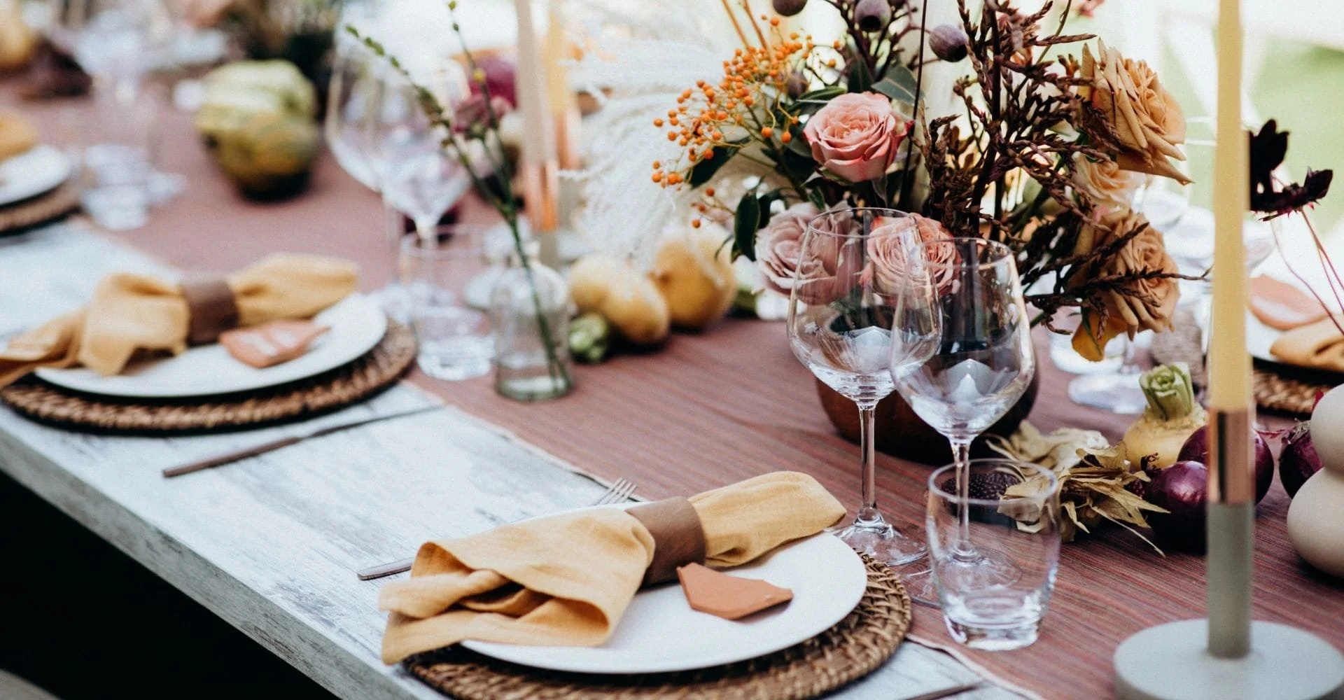 Elegant dining table set with woven placemats, folded beige napkins, wine glasses, and autumnal floral centerpiece, creating a cozy, festive atmosphere.