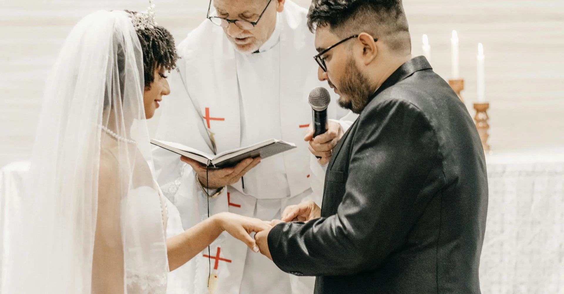 A couple exchanging vows during a wedding ceremony in a church, surrounded by floral arrangements and seated guests