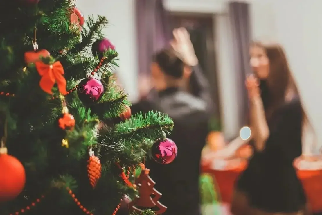 How to host a holiday party? Pretty image of tree and party guests in background.
