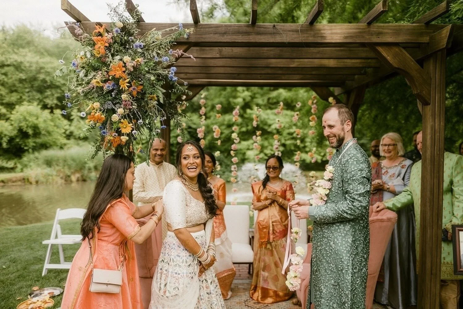 Guests celebrate an Indian wedding by the lake, surrounded by beautiful floral arrangements and traditional attire.