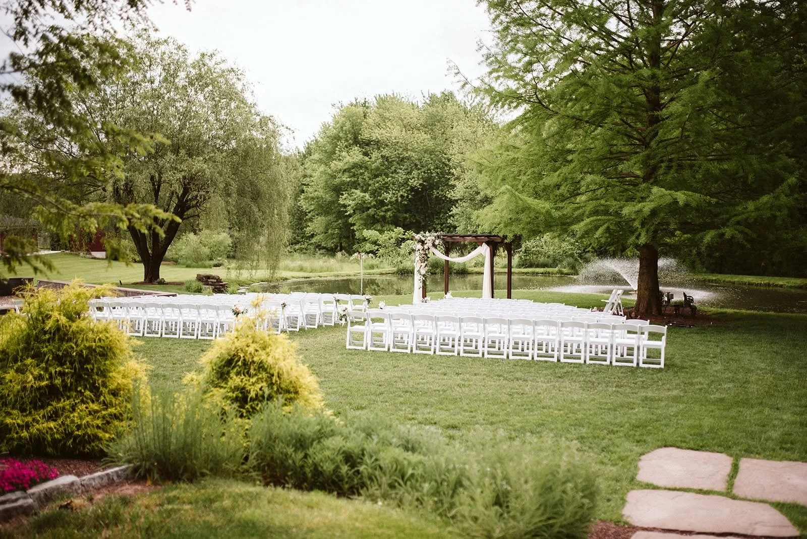 A beautiful outdoor wedding setup at a farm, featuring white chairs, floral arrangements, and a rustic archway.