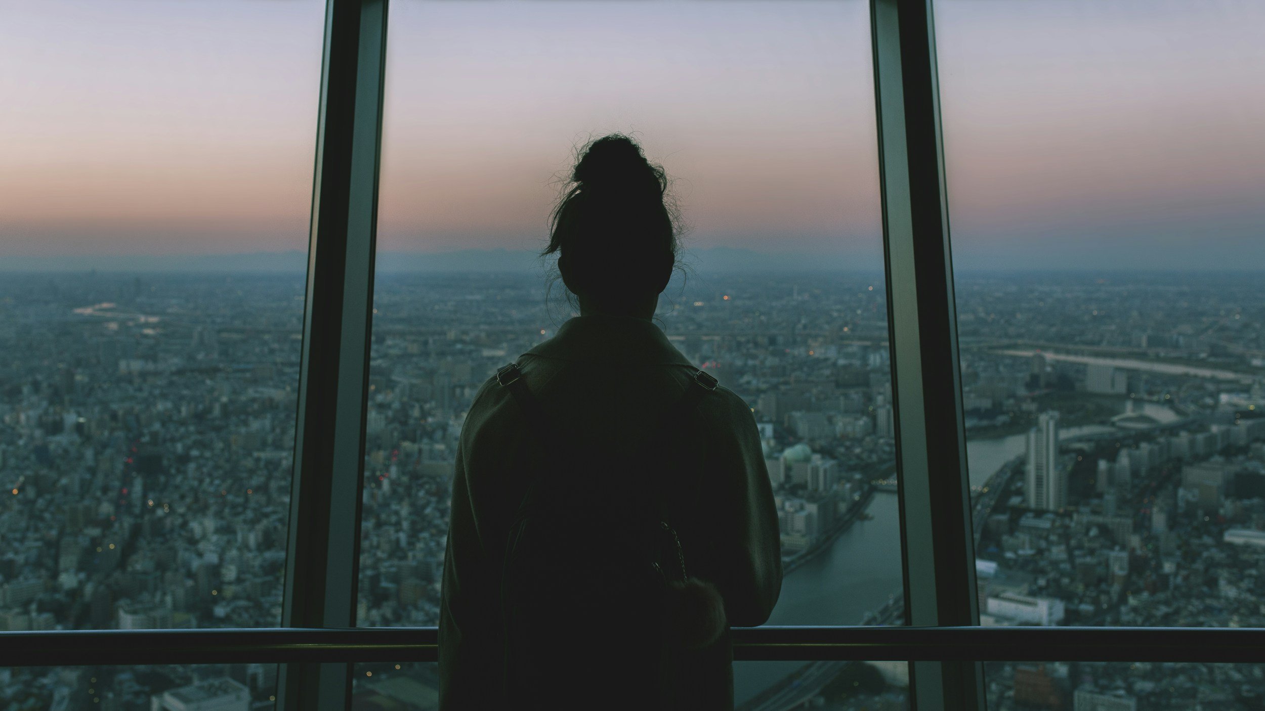 woman wearing backpack and looking out large window over city