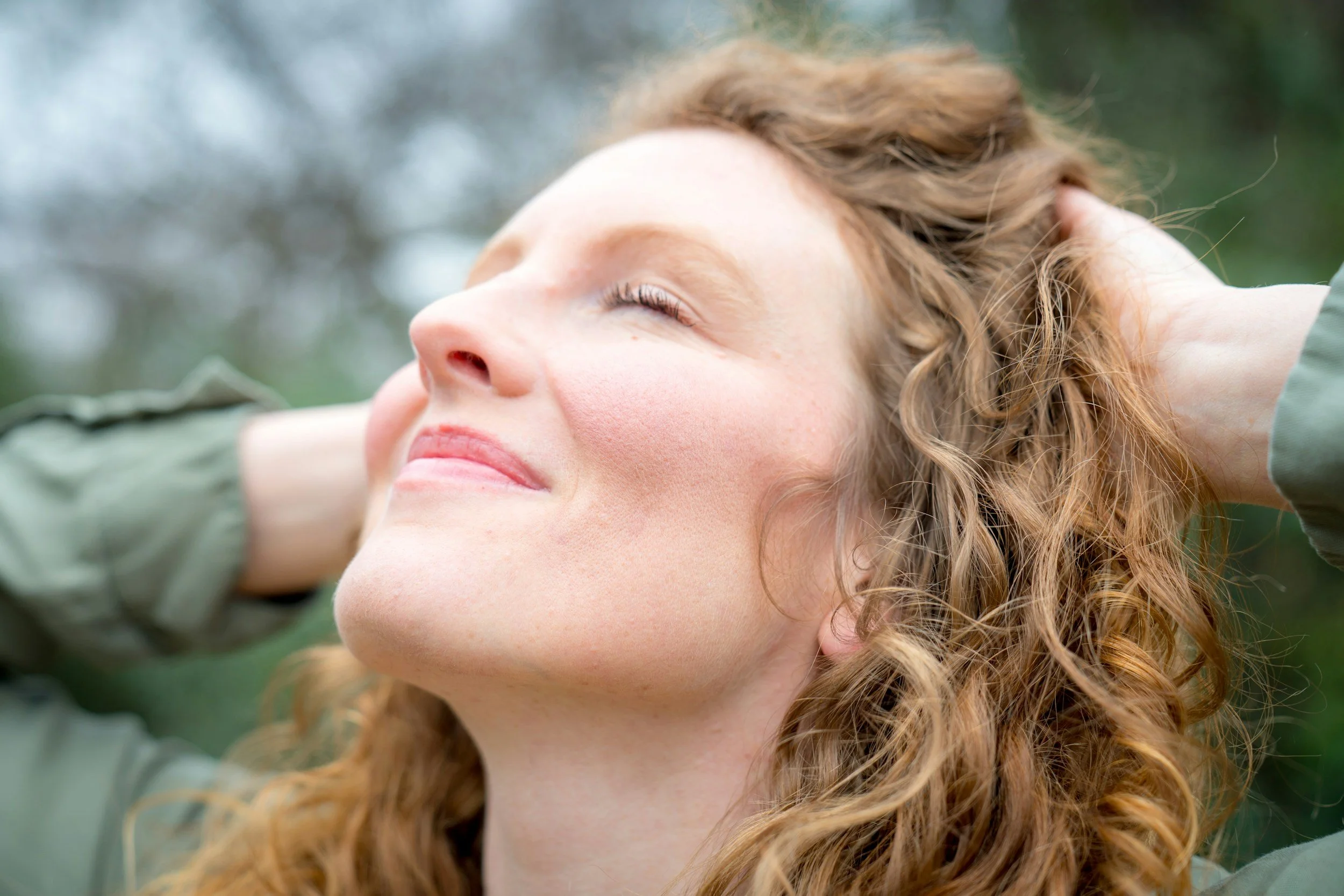 Woman outdoors with eyes closed, taking a deep breath and appearing calm and grounded