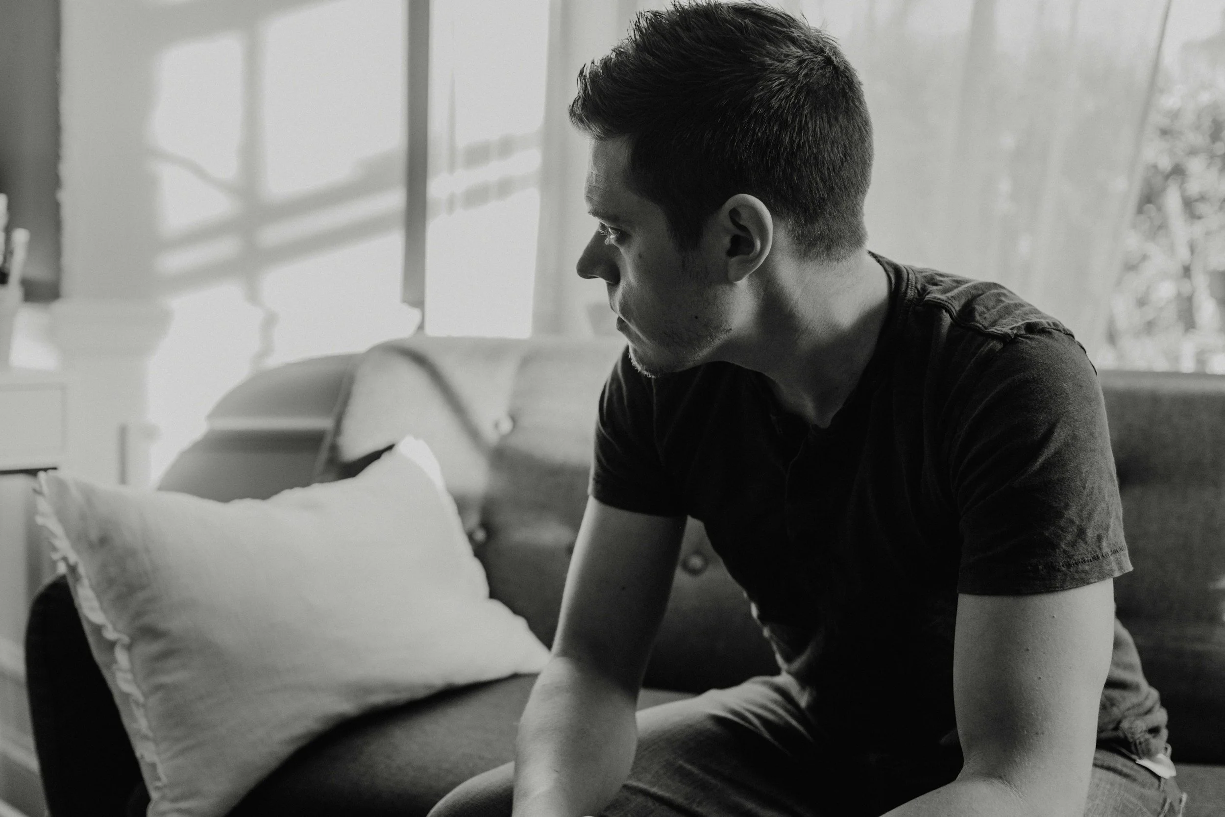 Man sitting on a couch and looking away in a black-and-white photo.