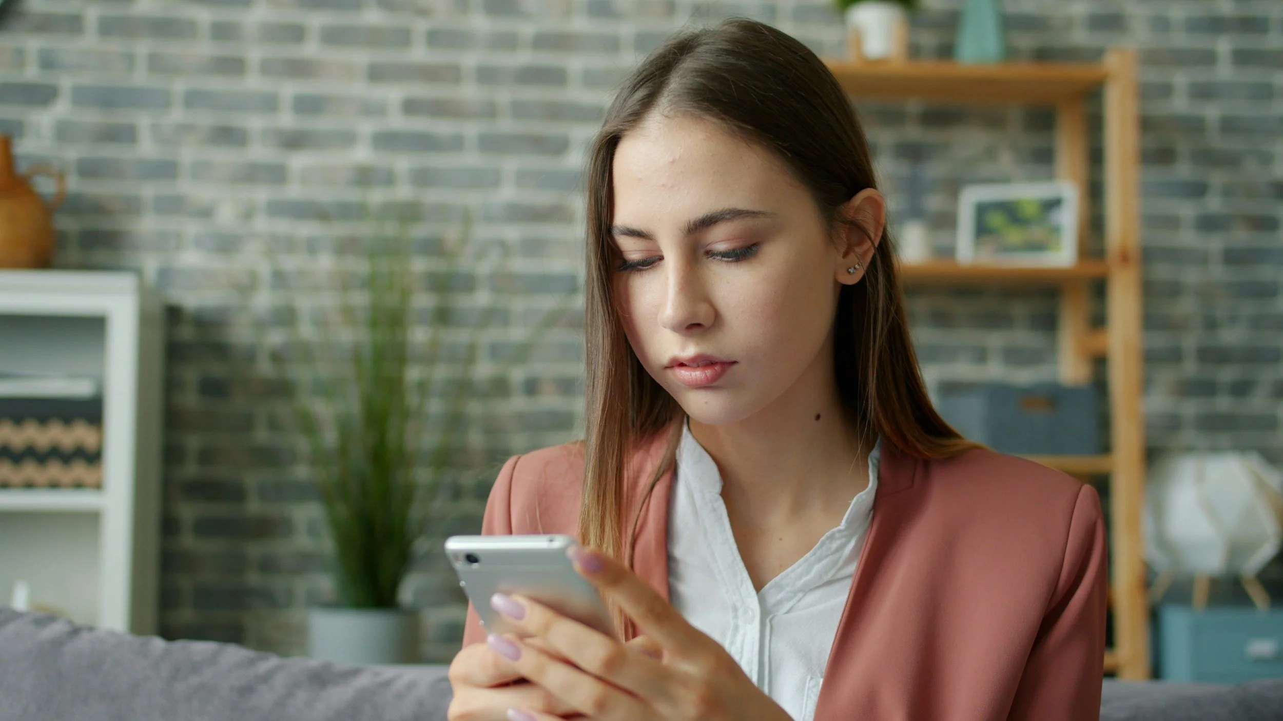 Woman looking down at her phone while sitting indoors.