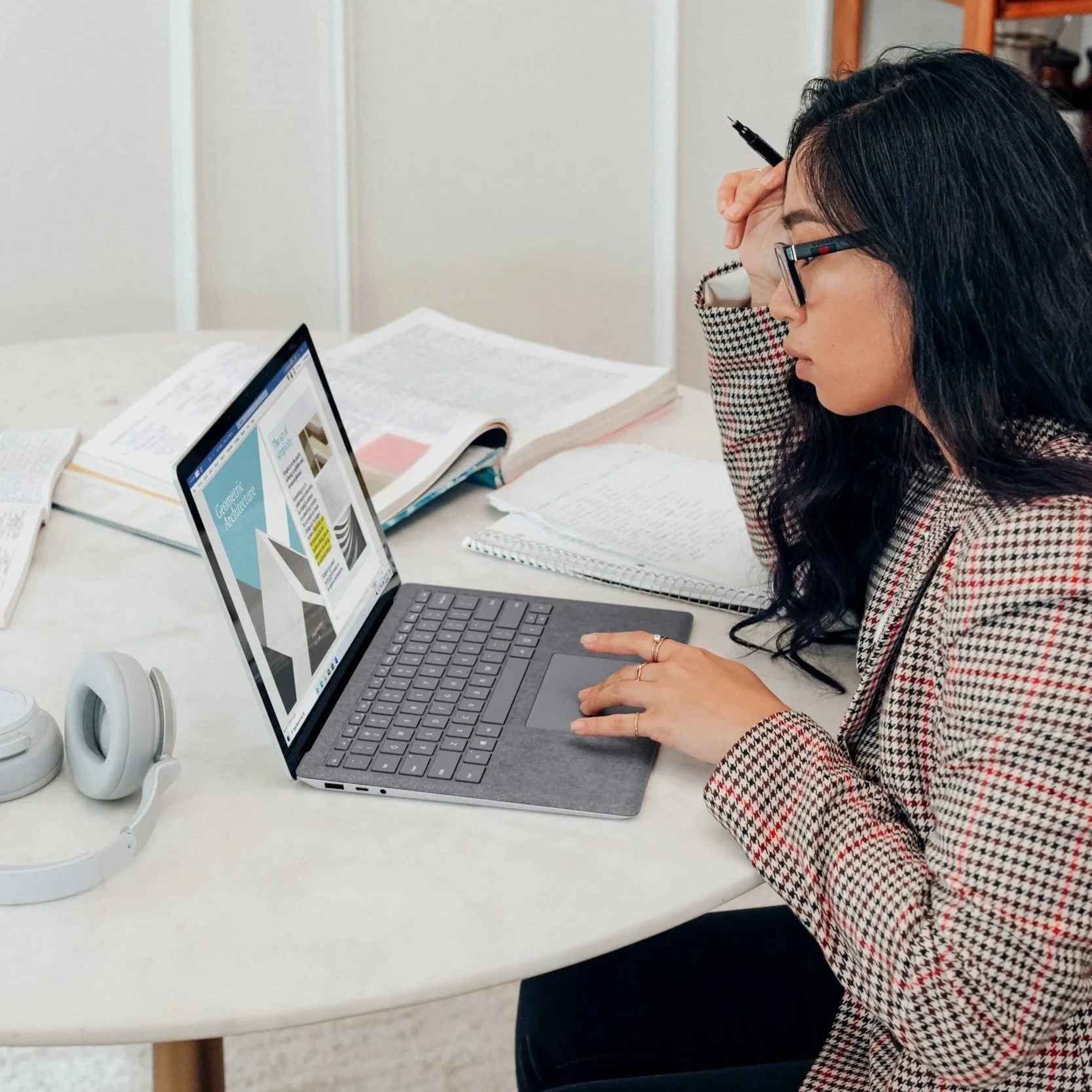 Woman working on a laptop with hand on forehead, appearing focused and overwhelmed