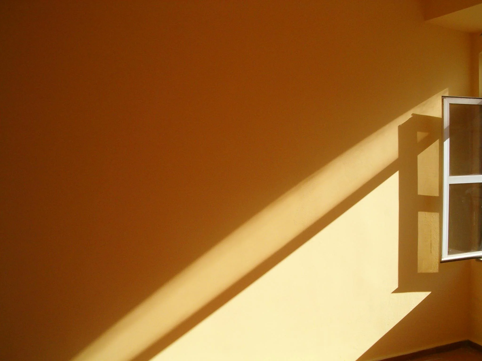 Sunlight casting diagonal shadows on a yellow wall near a partially open window.
