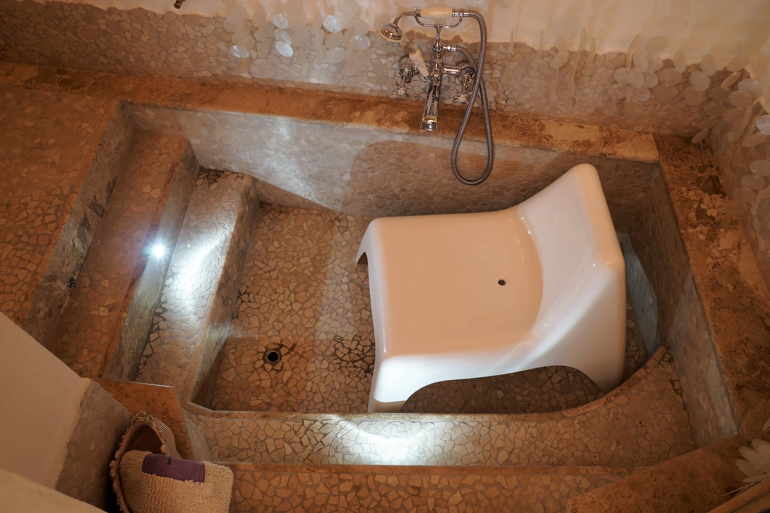 Vasca da bagno con rivestimento in mosaico, dotata di una vasca idromassaggio con forma moderna e angolare, facendo parte di un'area bagno elegante e ben illuminata.
