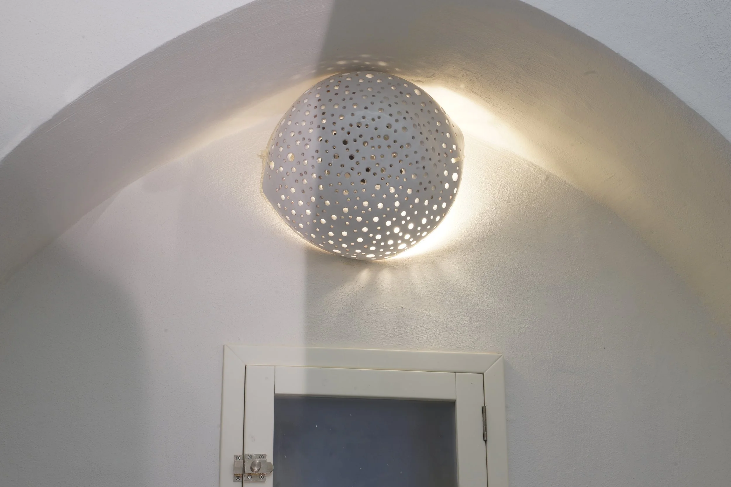 Applique da soffitto bianca a forma di sfera con fori che proietta luci sul soffitto e sulla parete
