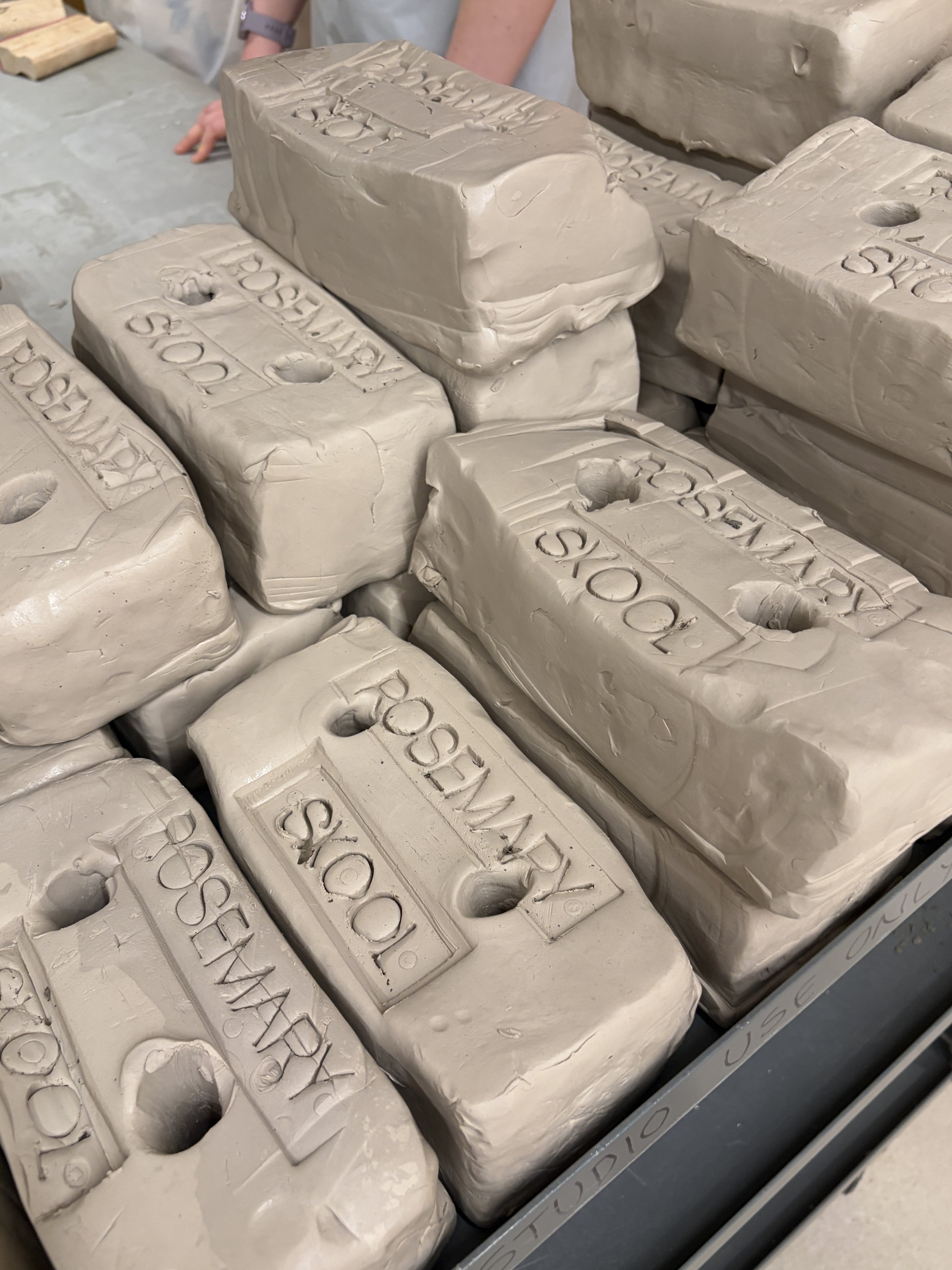 A close up image of a stack of wet clay bricks each stamped with ROSEMARY SKOOL