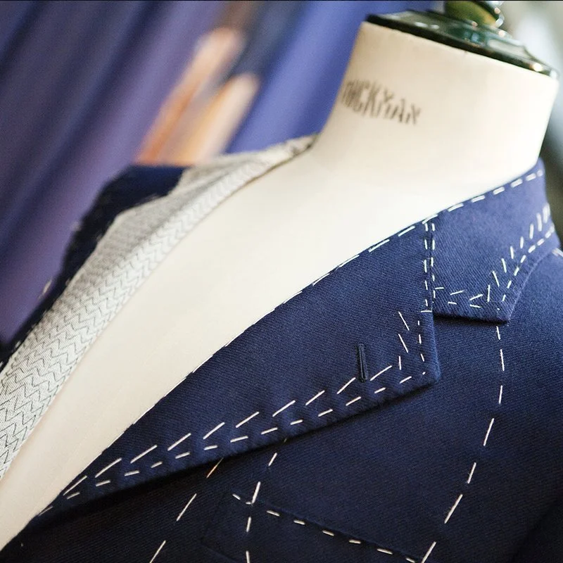 Close-up of a tailor mannequin wearing a navy custom suit with white stitching details, and part of a light-colored shirt with a subtle pattern visible underneath. Custom Clothing for Thompson's of Wilmington, a Men’s clothing store in Wilmington NC.