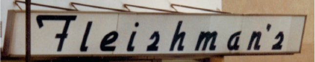 Sign with black cursive text that reads 'Fleishman's' on a white background with a brown border. Lineage of Thompson's of Wilmington, a Men’s clothing store in Wilmington NC.