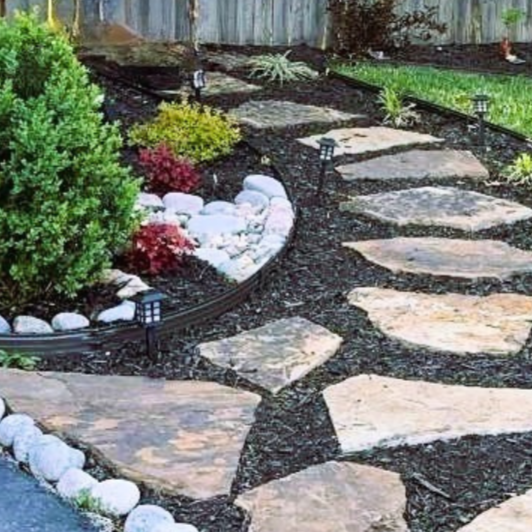 Stone pathway in a landscaped garden with small solar lights, plants, and mulch.