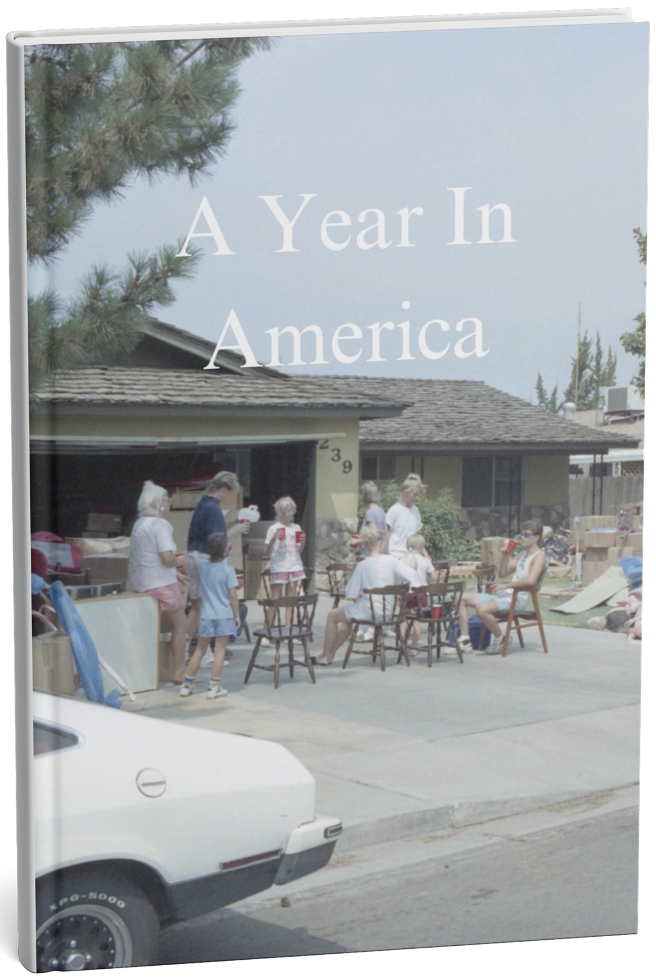 A book titled "A Year In America" with a cover photo of a yard sale in front of a house, featuring people browsing and sitting outside.
