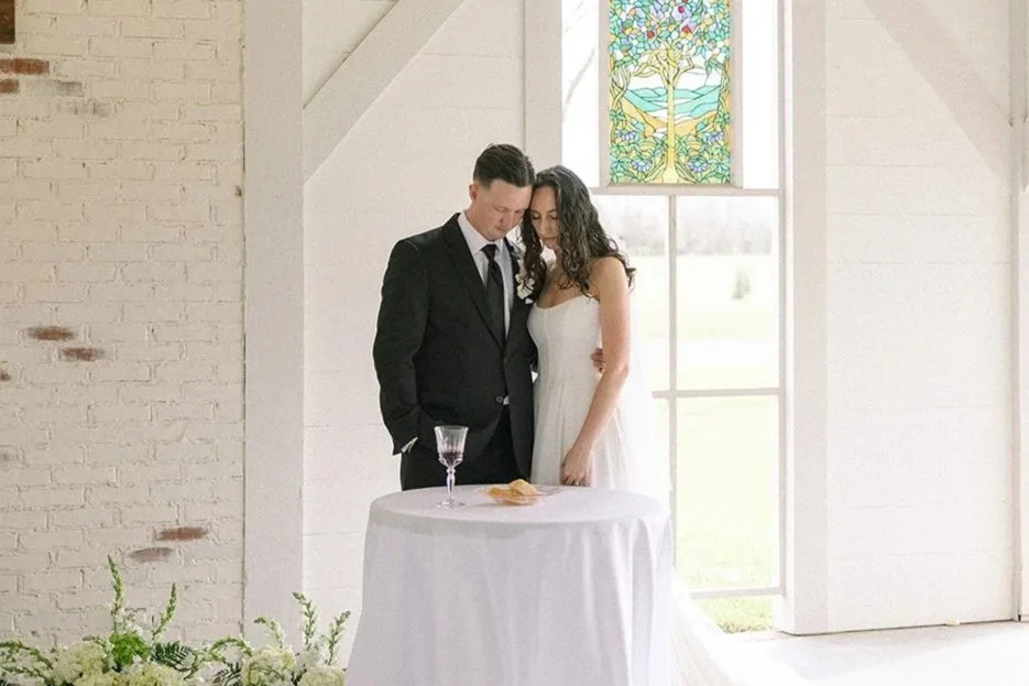 A bride and groom stand together in a chapel praying before communion during a wedding ceremony.
