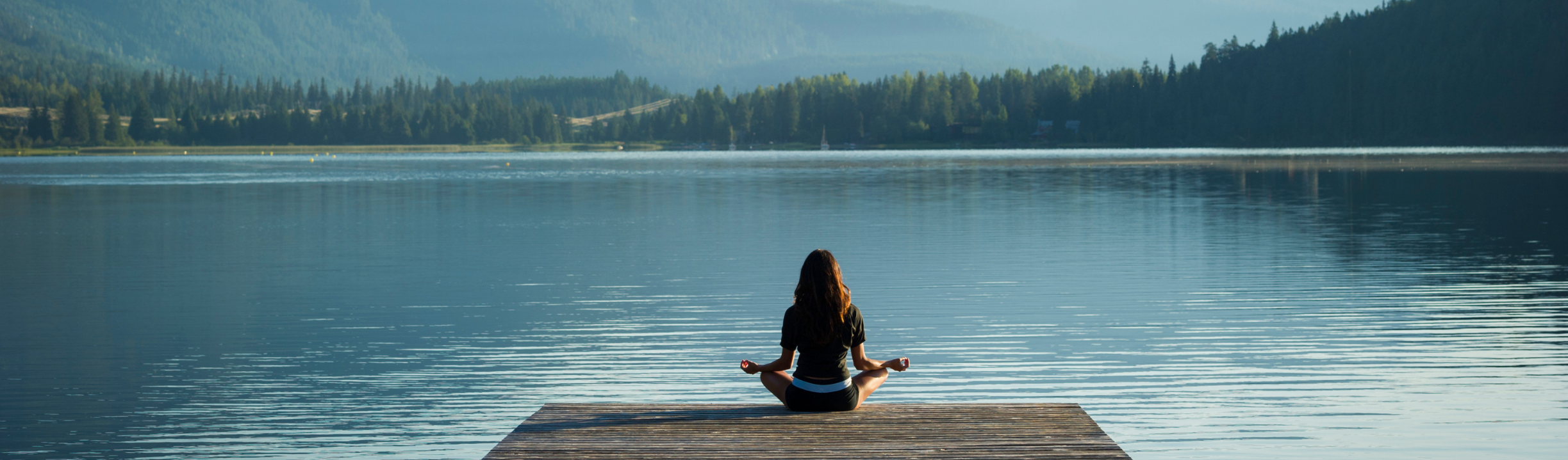 A woman meditating on a dock by a lake to practice self-regulation