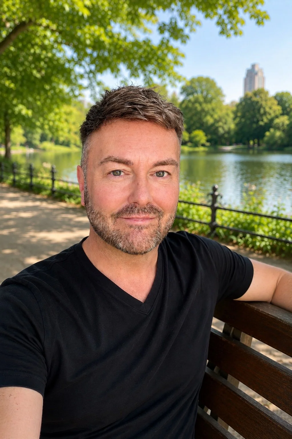 Lewis Mabee sits on a park bench surrounded by trees and a peaceful lake, enjoying a quiet moment of reflection in natural light, conveying calm, balance, and emotional wellbeing.