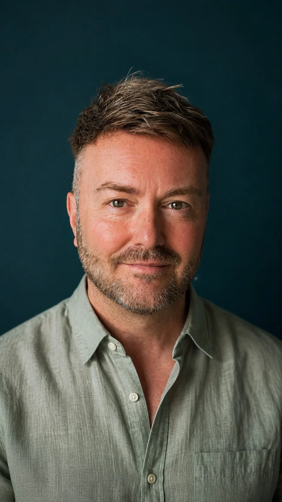 Lewis Mabee looking directly at the camera with a calm, confident expression against a deep teal background, conveying intuition, trust, insight, and spiritual guidance.