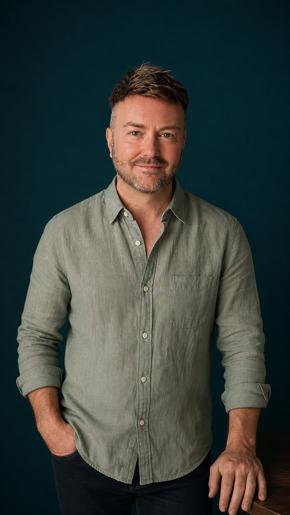 Lewis Mabee standing confidently against a deep teal background with a warm, welcoming expression, creating a sense of trust, safety, and readiness for a personal psychic reading or spiritual guidance session.