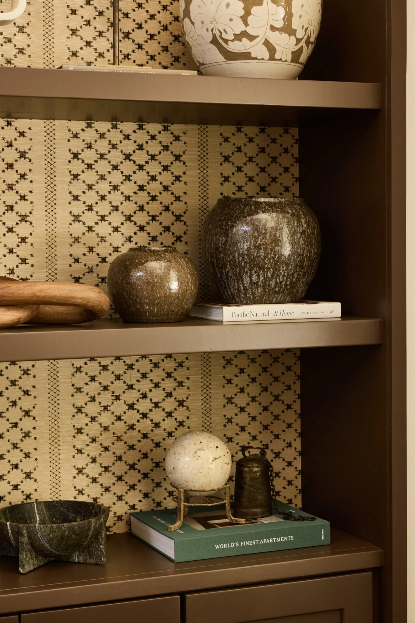 Shelf showcasing decorative vases, a carved stone bowl, and books against black and beige patterned wallpaper.