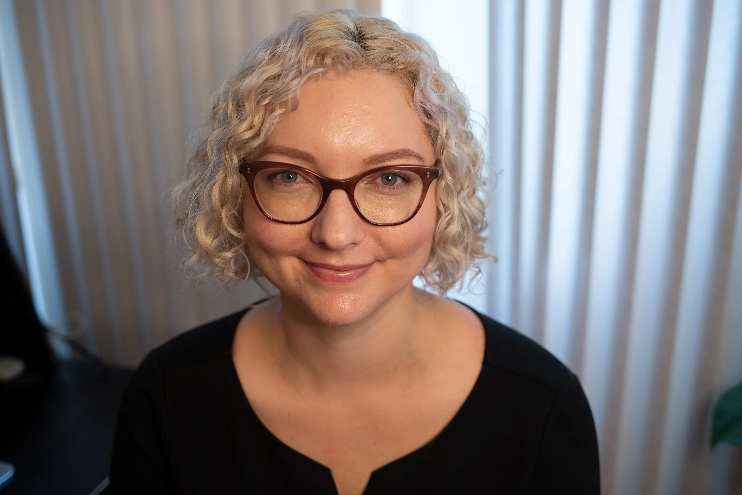 Alice Rizzi headshot, brown glasses, black dress, blonde hair