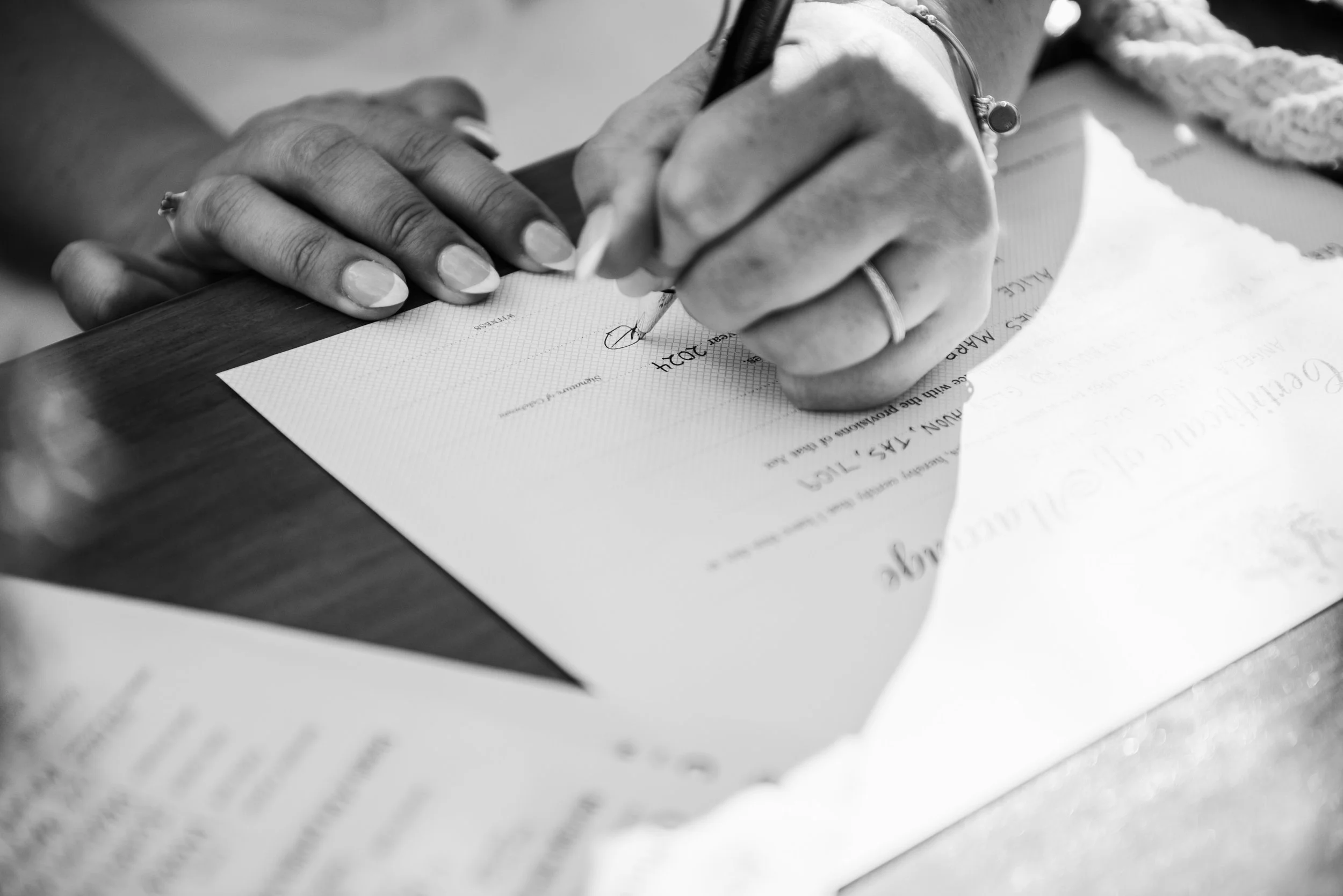 Close-up of a person’s hands signing a document with a pen, with paper and printed text visible.