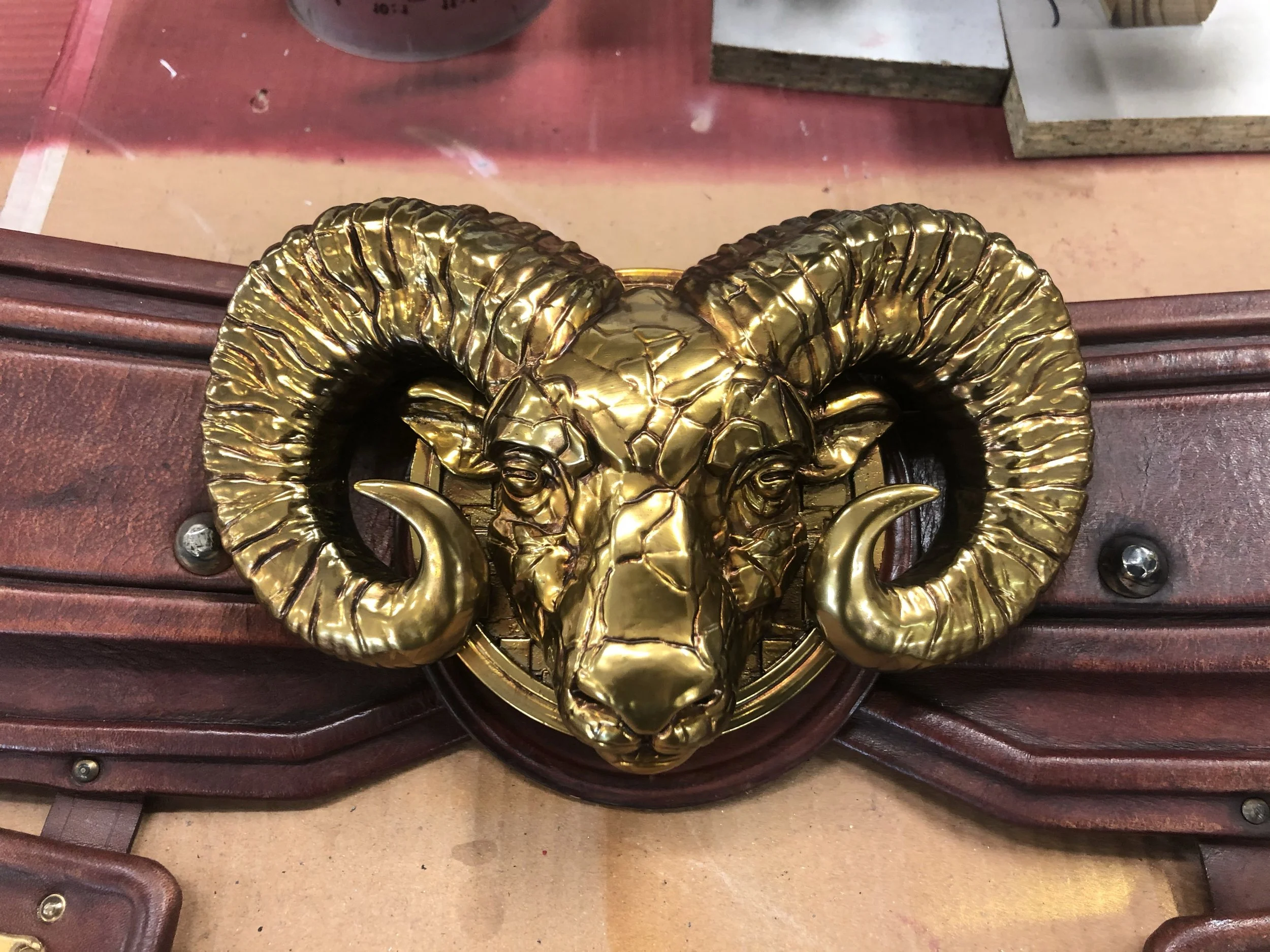 A gold-colored ram's head wall decor with large curled horns mounted on a wooden surface.
