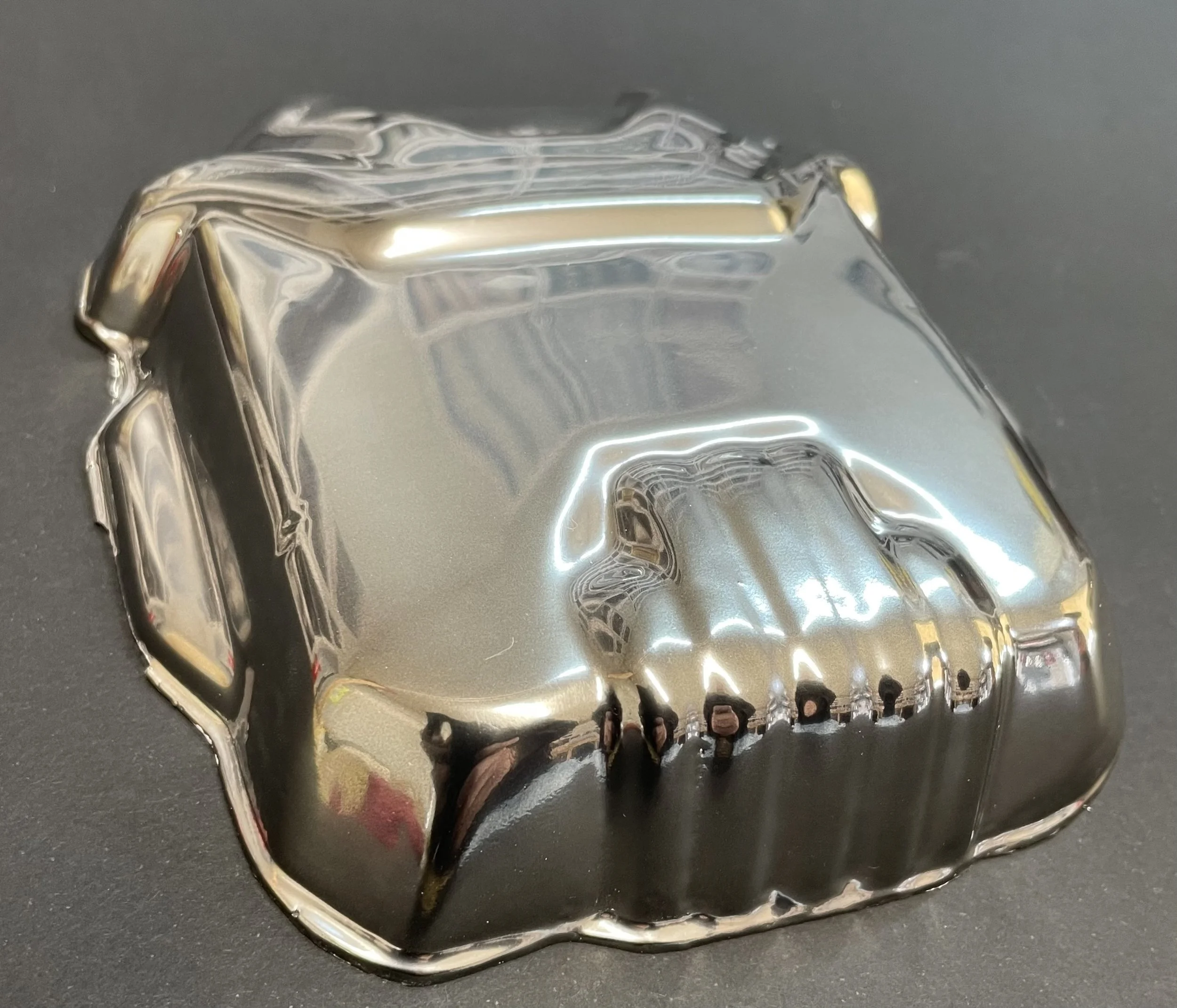 A shiny, reflective object with a jewel-like shape, metallic surface, and jagged edges on a dark background.