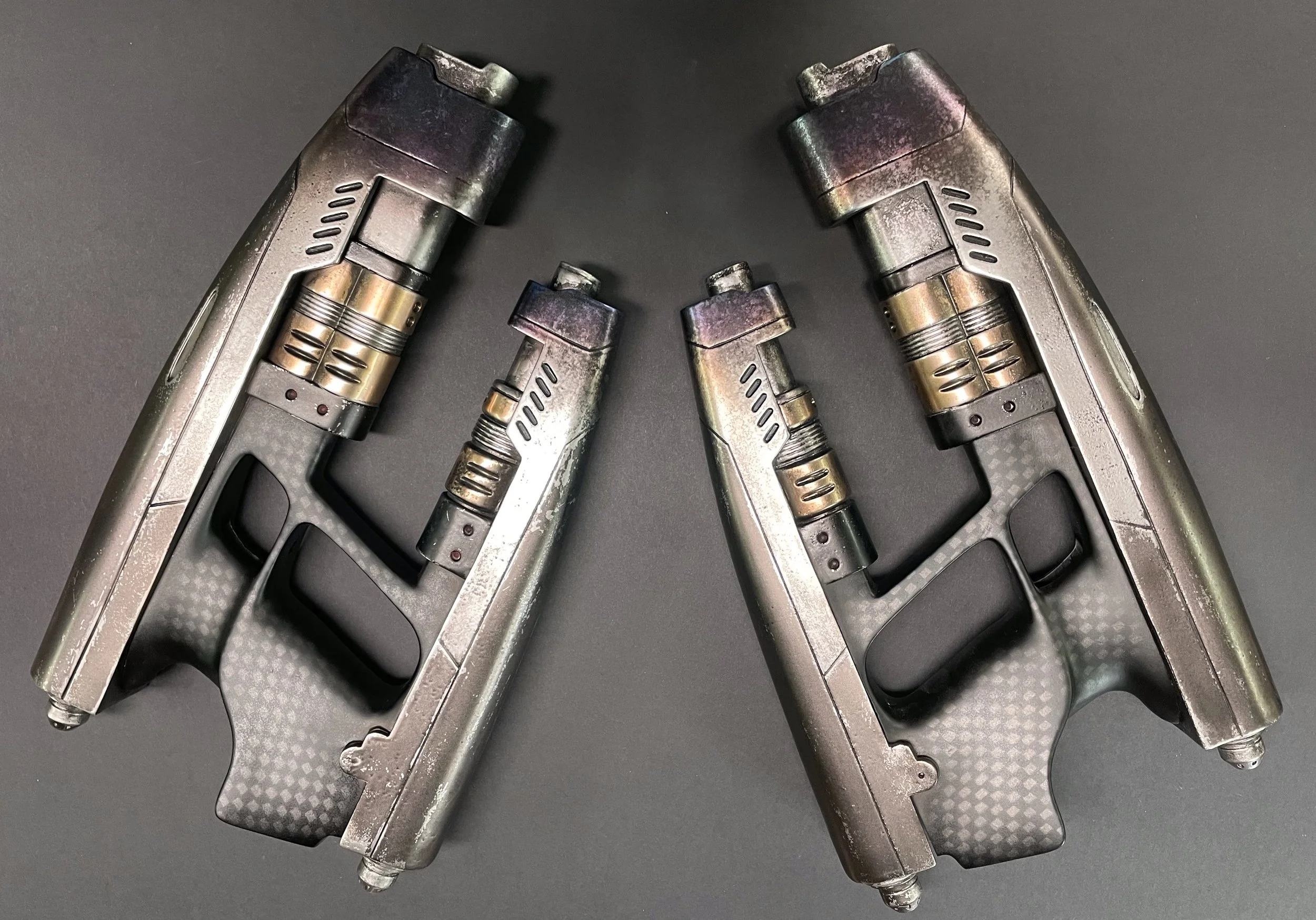 Two silver and black futuristic laser guns with metallic accents, positioned facing each other on a black surface.