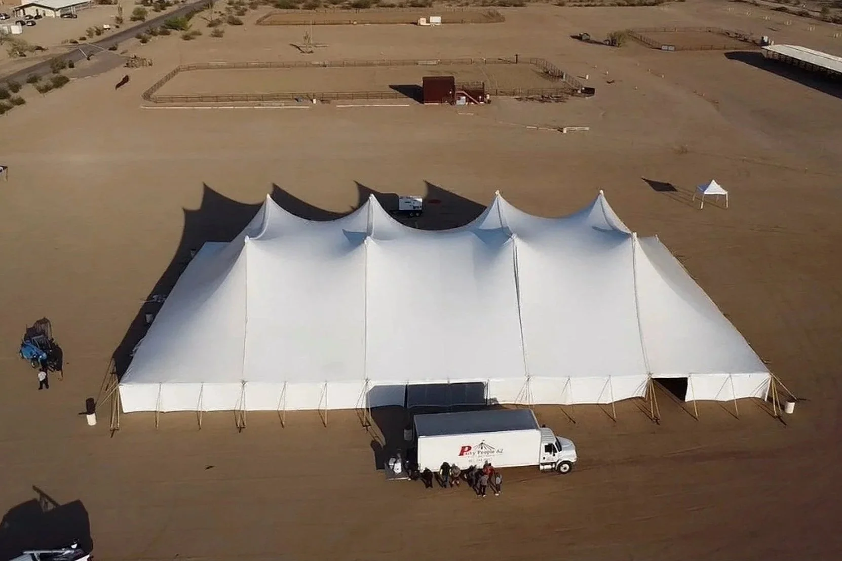 Large white event tent set up in a barren desert landscape with vehicles and small structures nearby.