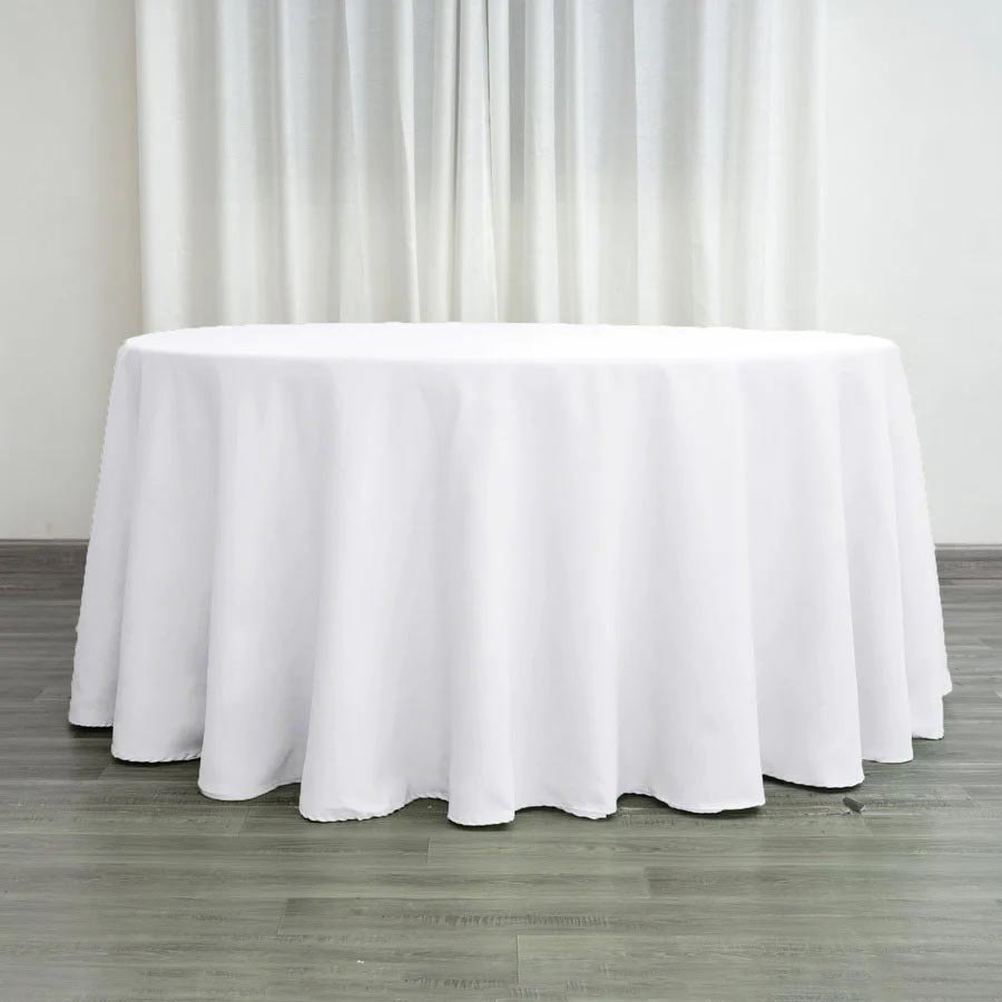 Empty round table covered with a white tablecloth in front of curtains