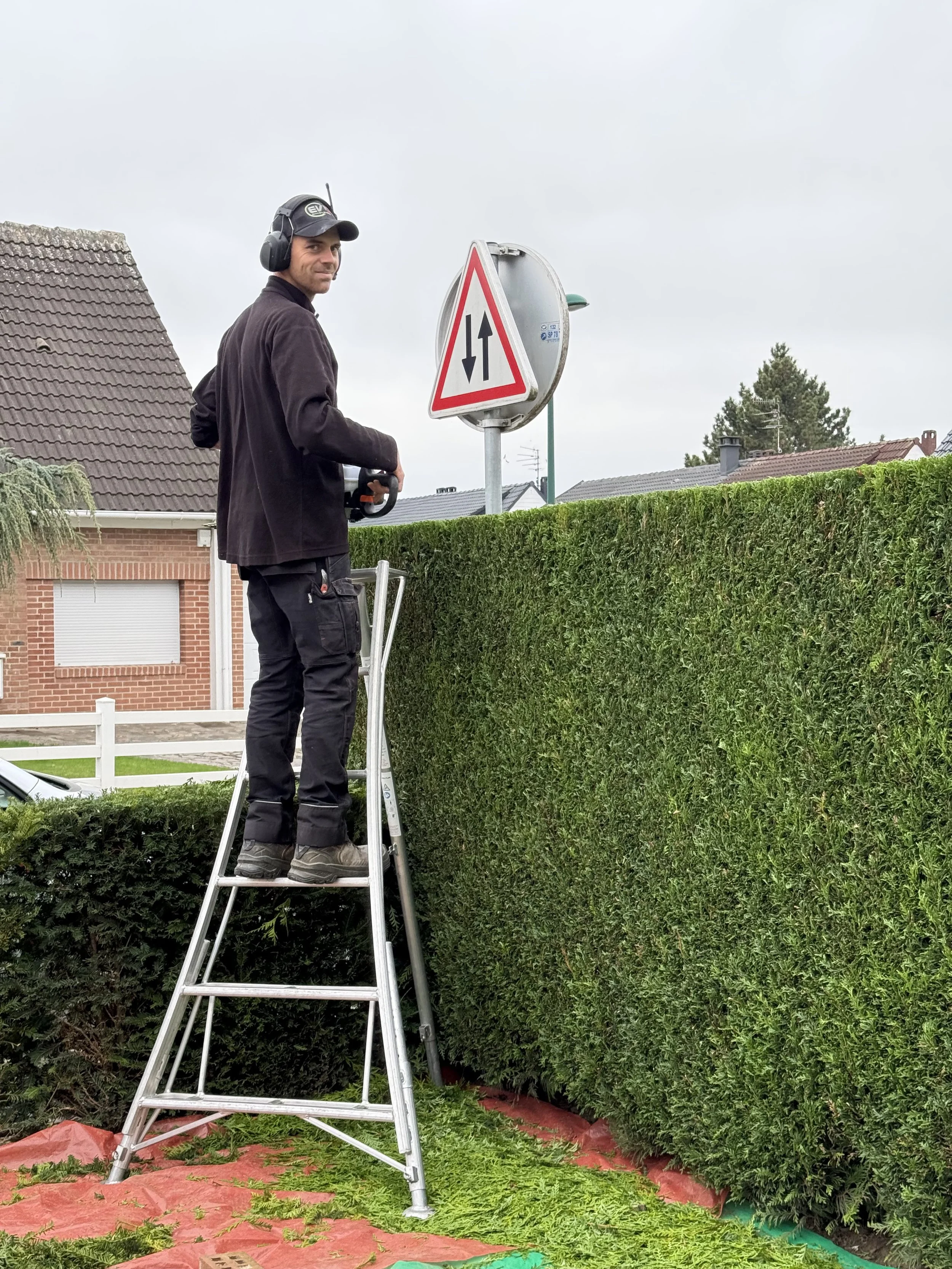 Un homme travaillant en hauteur sur une échelle devant un panneau de signalisation routière dans une zone résidentielle.