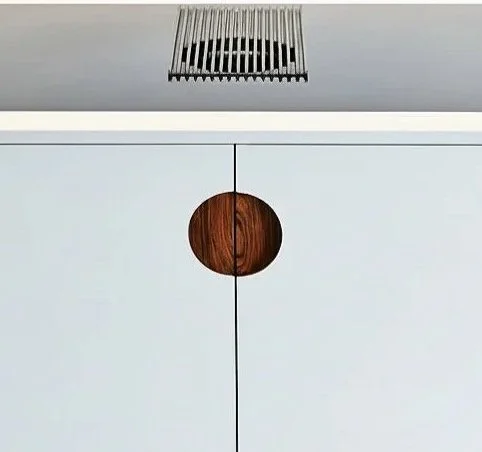 Close-up of a cabinet with a round wooden handle on white doors, positioned under a modern ceiling light fixture.