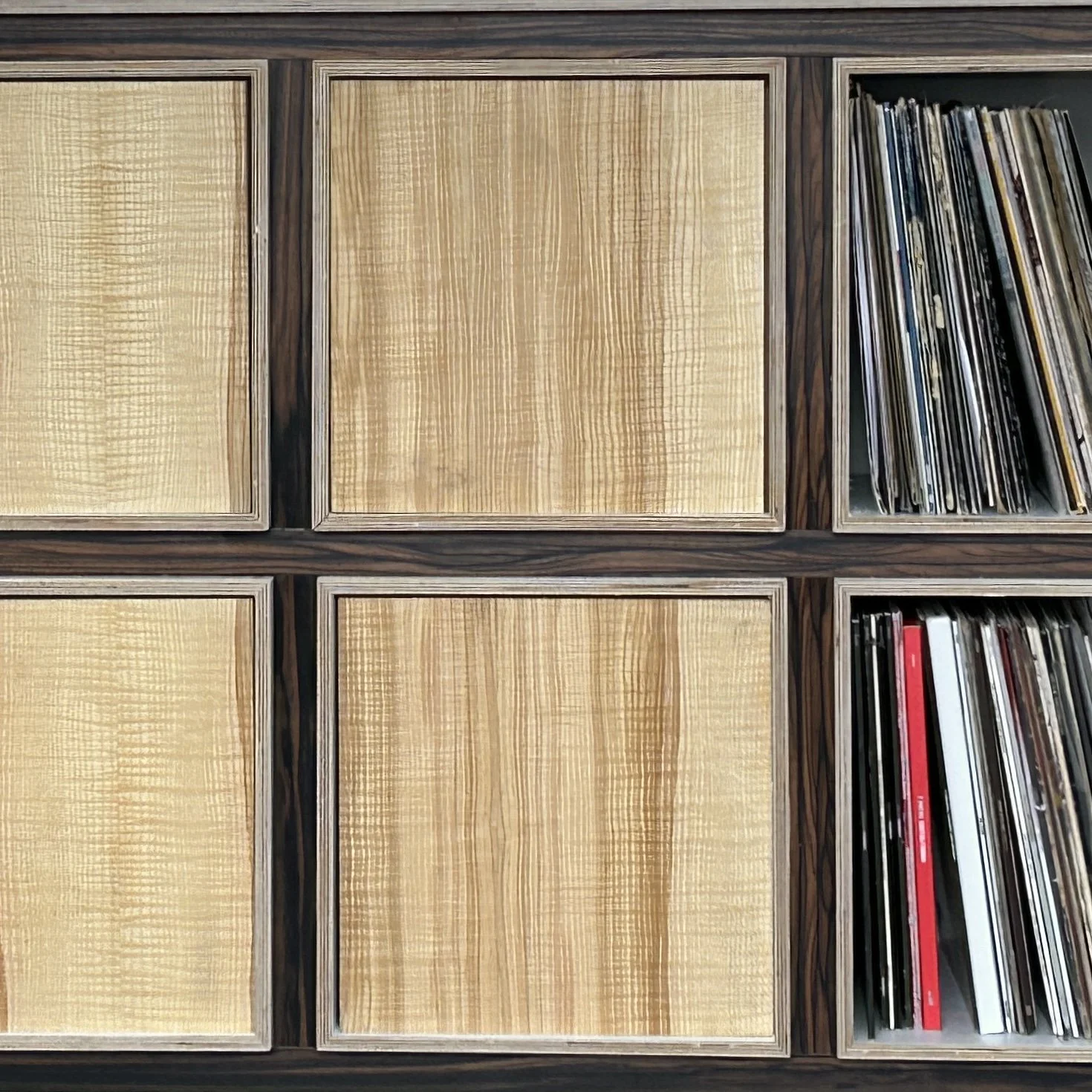 A section of a wooden cabinet with four empty square compartments and one compartment filled with vinyl records.