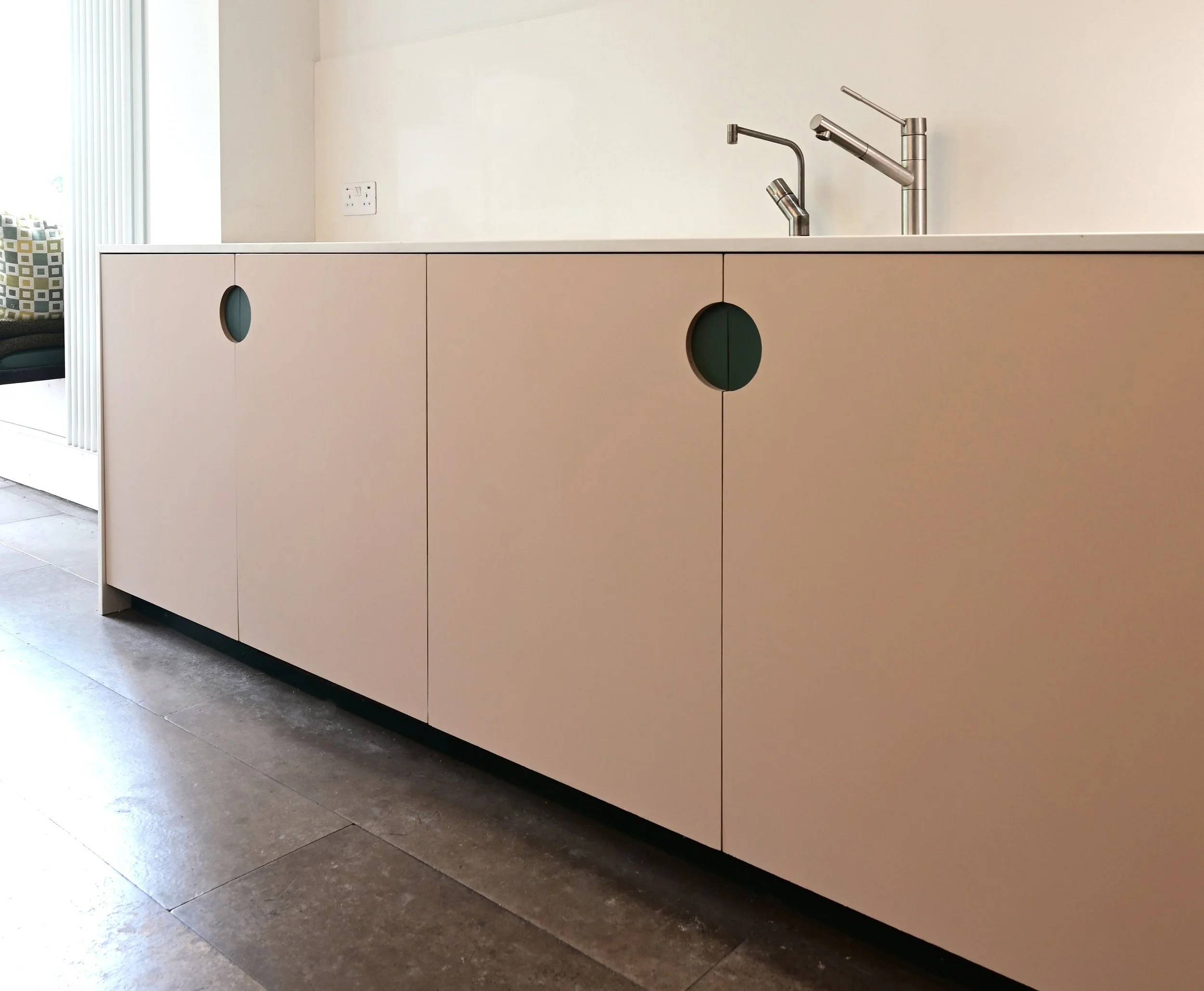 Modern kitchen with a beige cabinet under a white countertop and two stainless steel faucets.