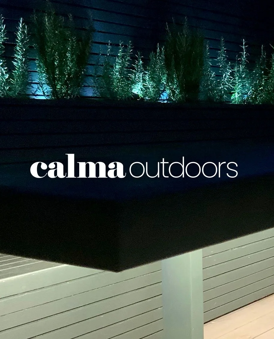 A close-up of a sign that reads 'calma outdoors' with a background of green plants illuminated by blue-green lighting.
