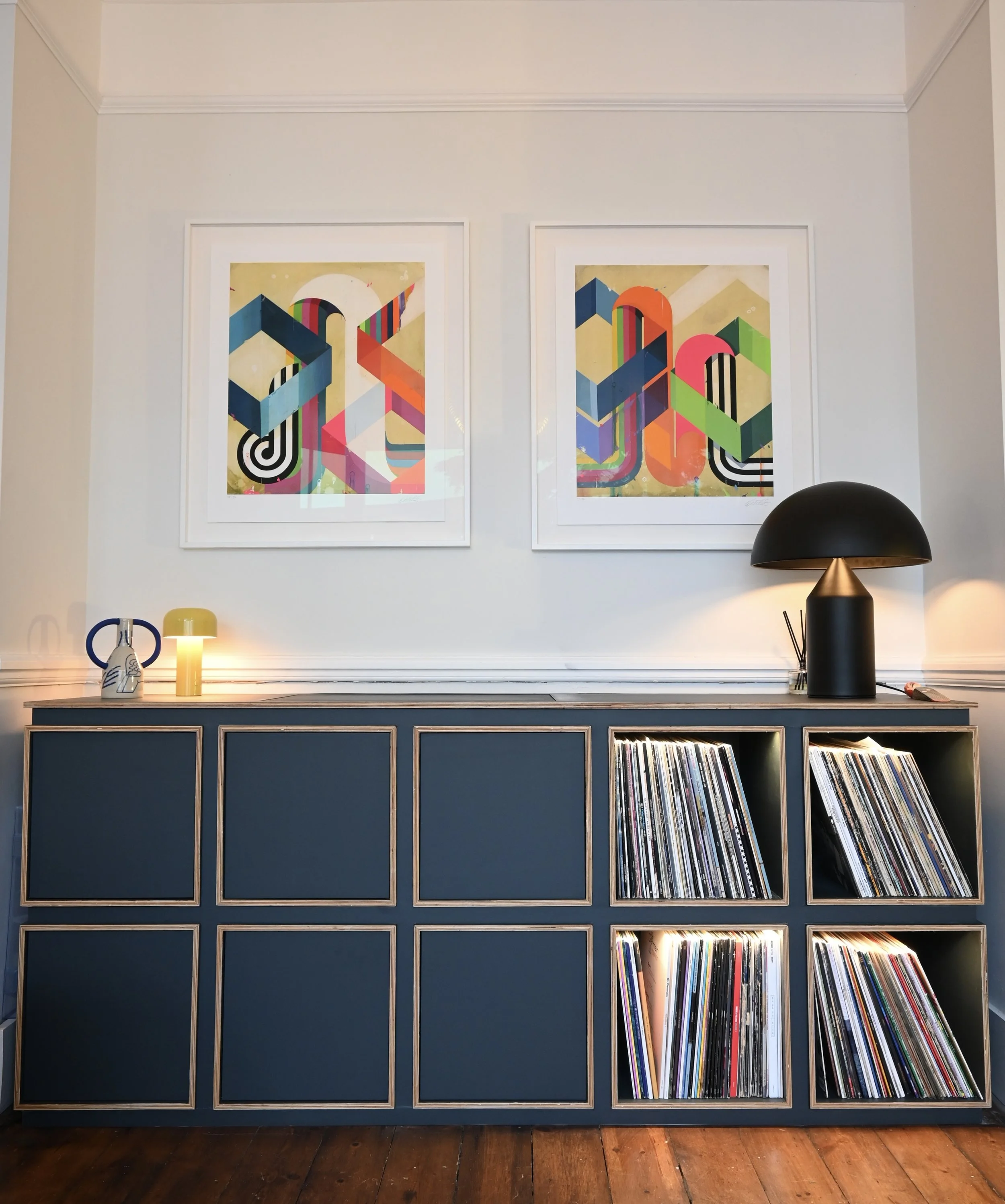 A blue cabinet with a grid design on the front, topped with decor items and a lamp, with two colorful abstract art prints on the wall above.