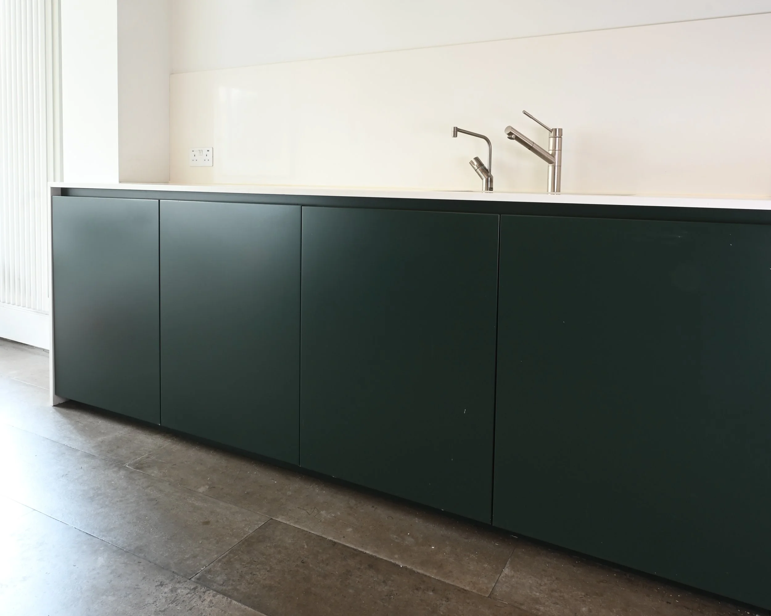 Modern kitchen with dark green cabinets, white countertop, and two silver faucets.