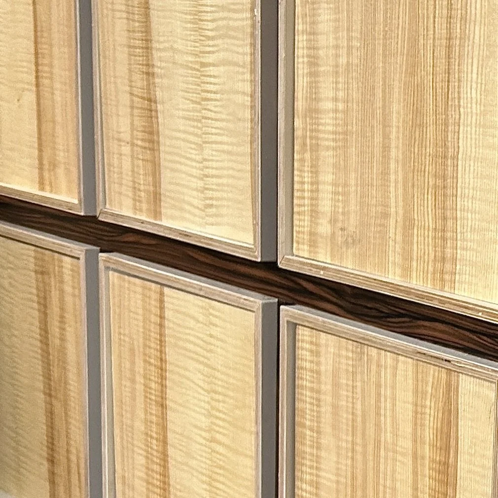 Close-up of a wooden cabinet with light-colored grain, framed with gray trim, featuring a dark horizontal accent strip.