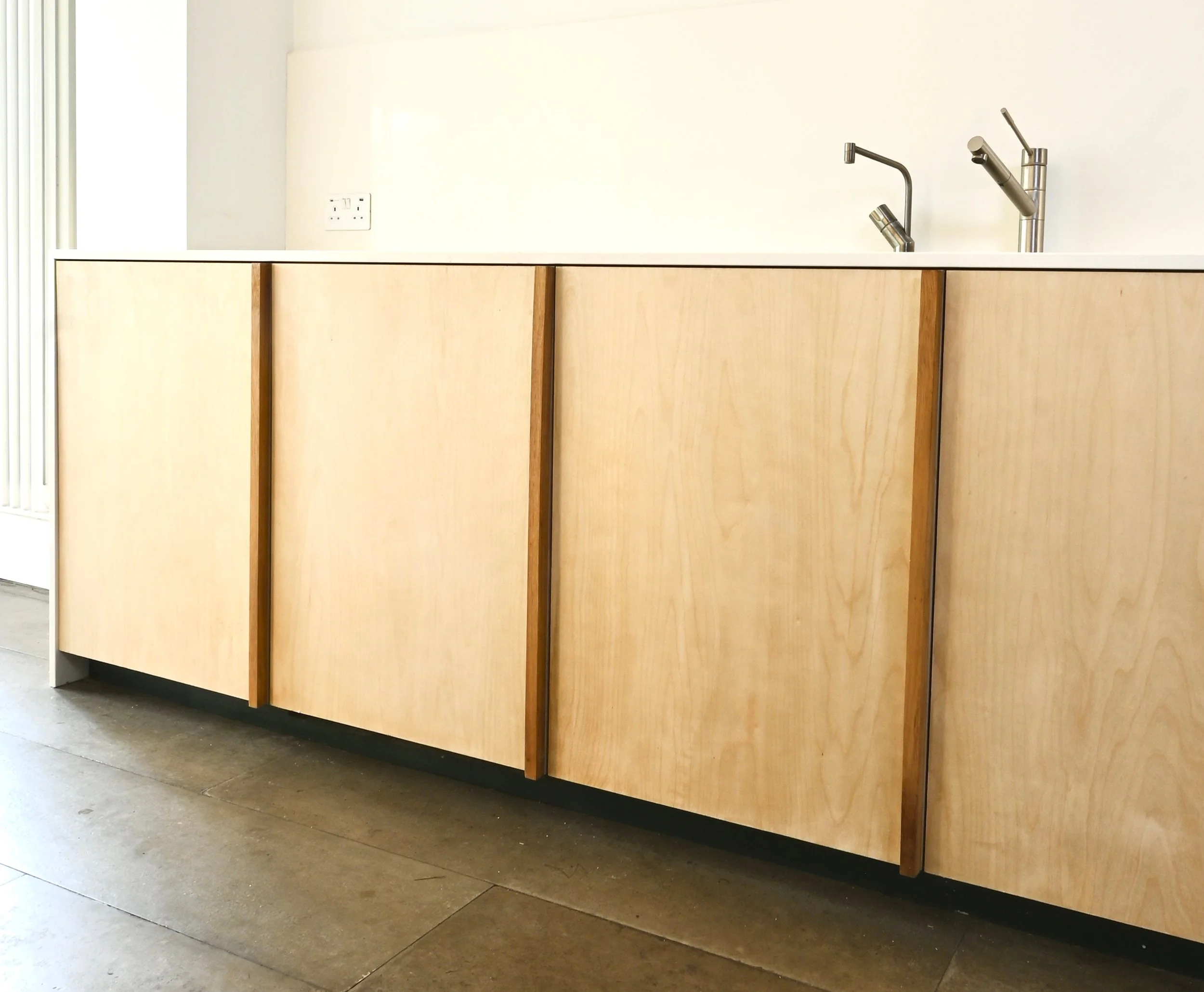 Kitchen with light wood cabinets, a white countertop, and modern silver faucets.