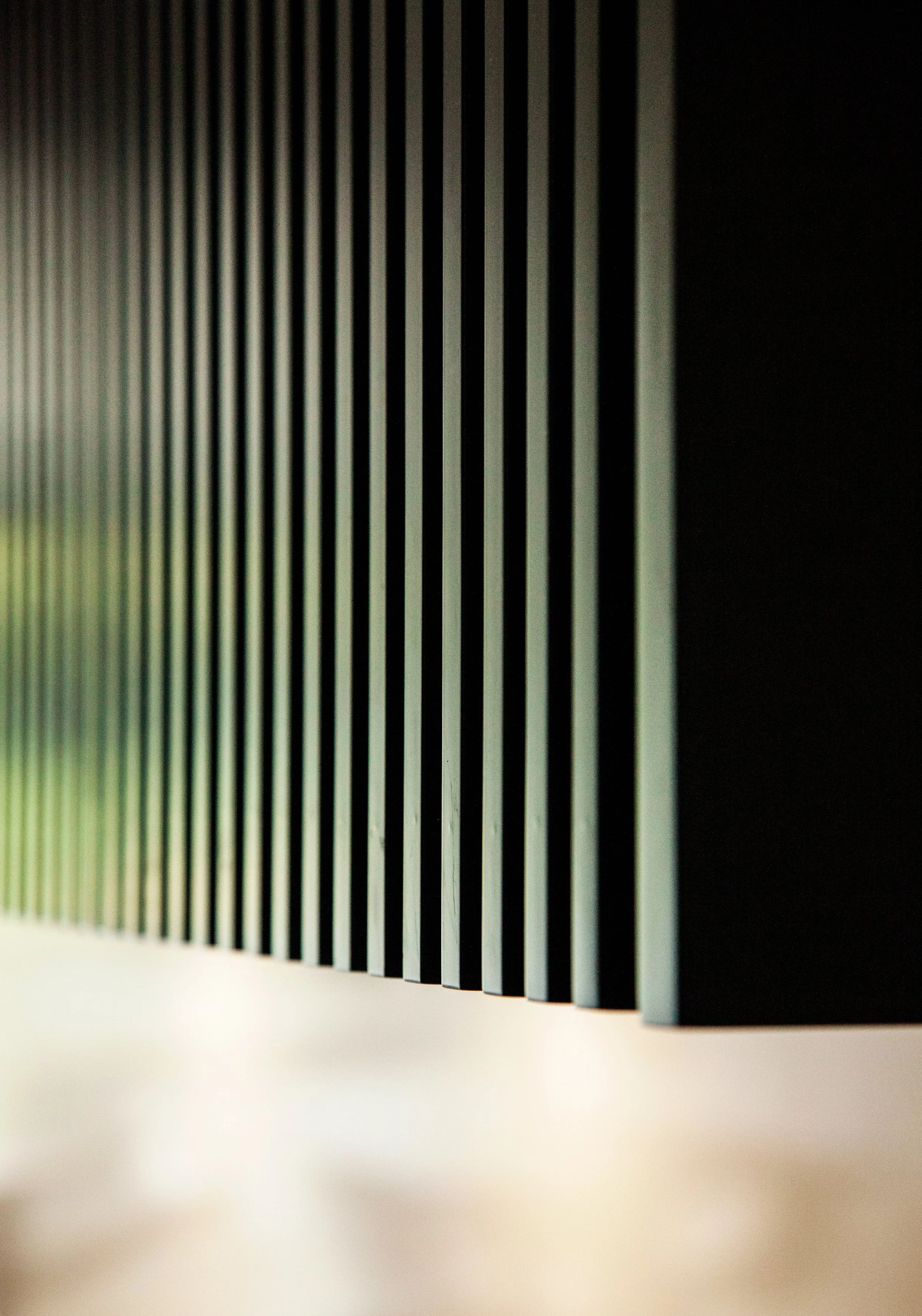 Close-up of vertical black slats or bars against a dark background, with a blurred light source at the bottom.