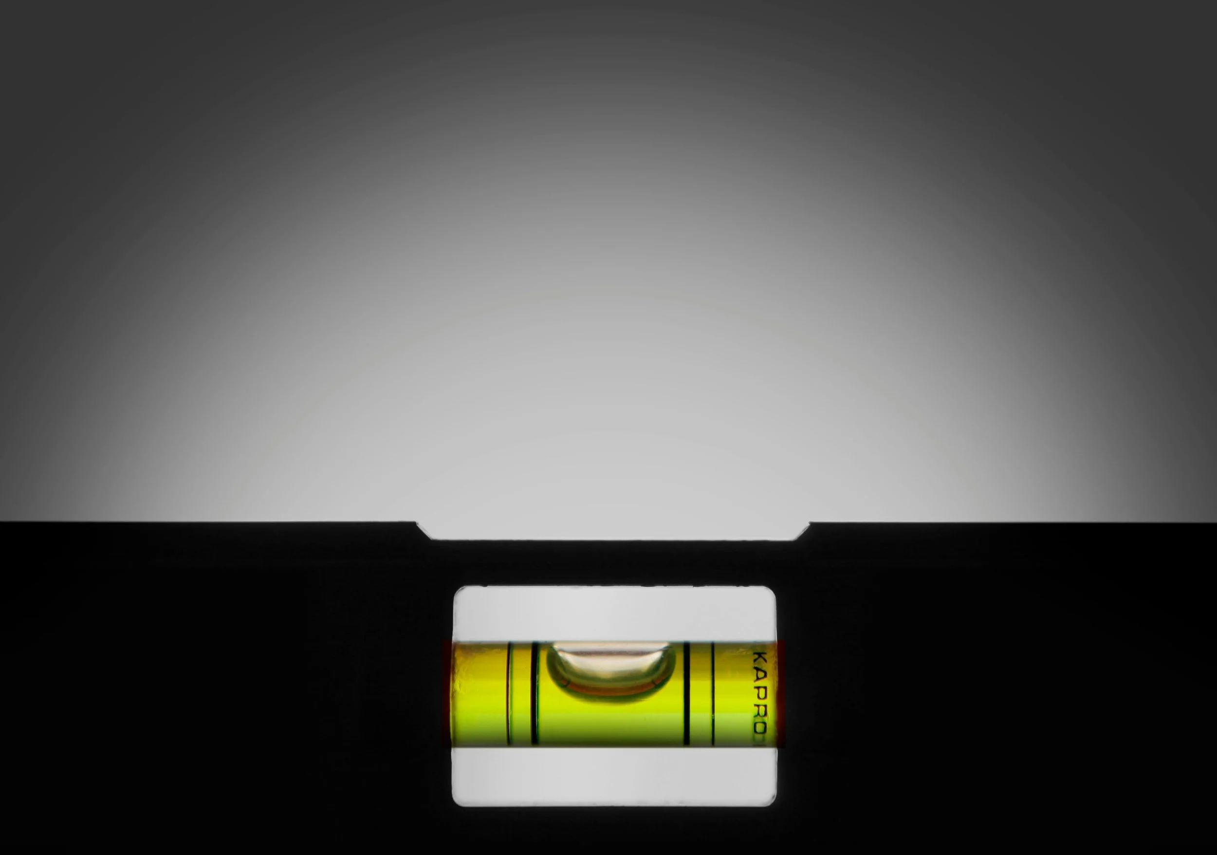 Close-up of a spirit level tool with a yellow and green liquid-filled vial, mounted on a black surface, against a gradient gray background.