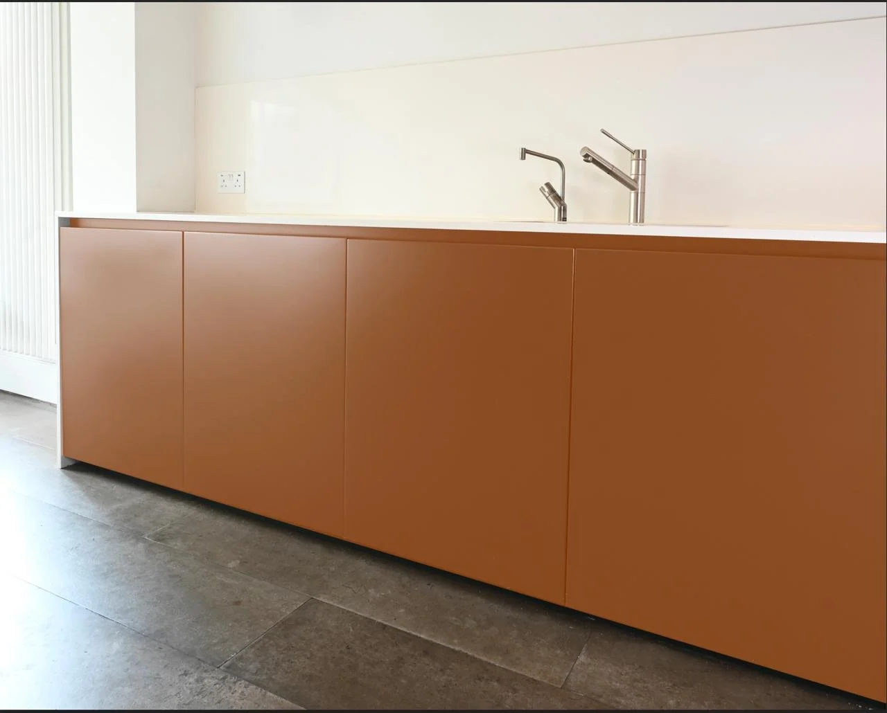 Modern kitchen cabinet with brown finish, white countertop, and dual silver faucets in a minimalist kitchen setting.
