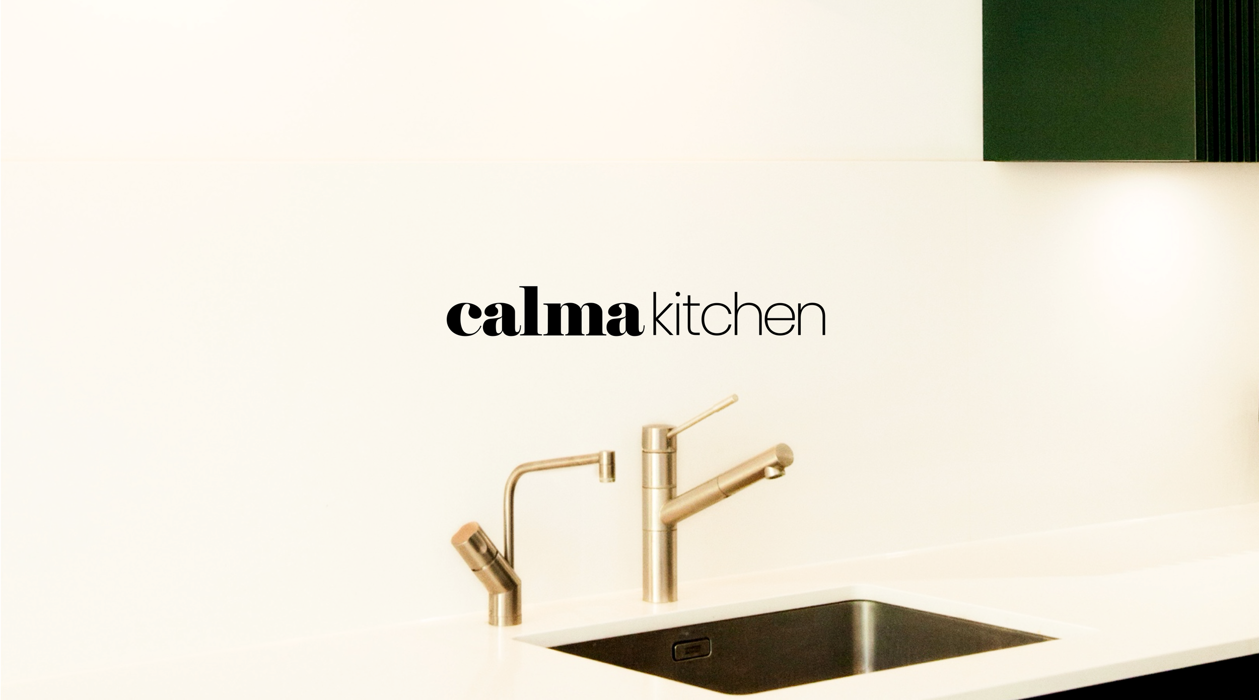 Modern kitchen sink with a two-tone faucet and black basin, with the words 'calma kitchen' on the white wall above.